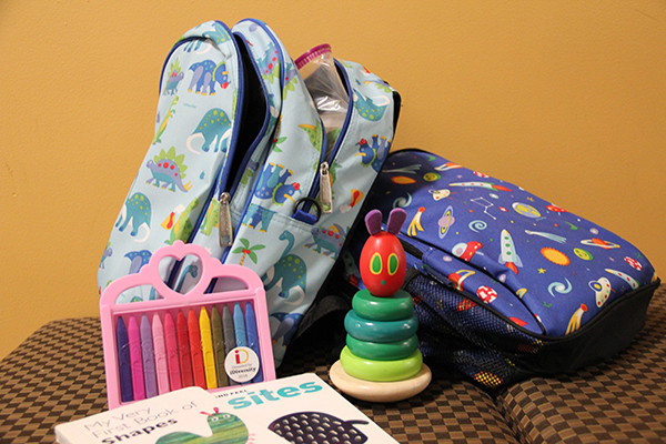 Children's backpacks displayed with books, a stacking toy, and crayons
