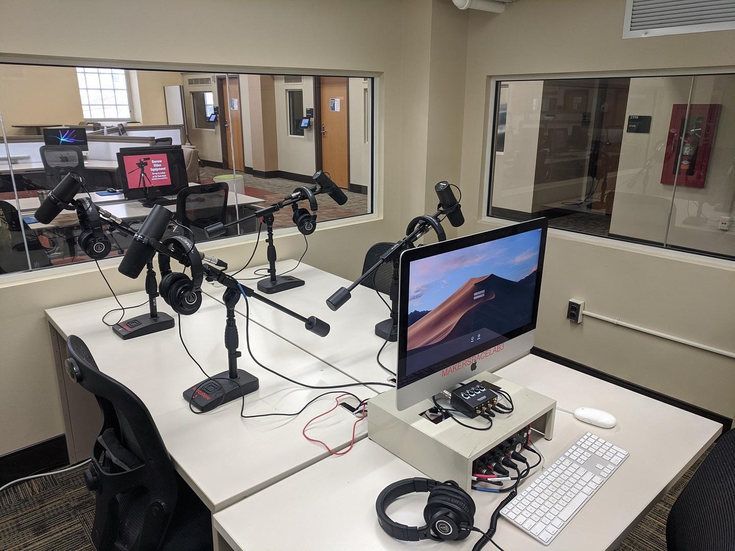 four microphones and a computer arranged on tables in the podcasting lab