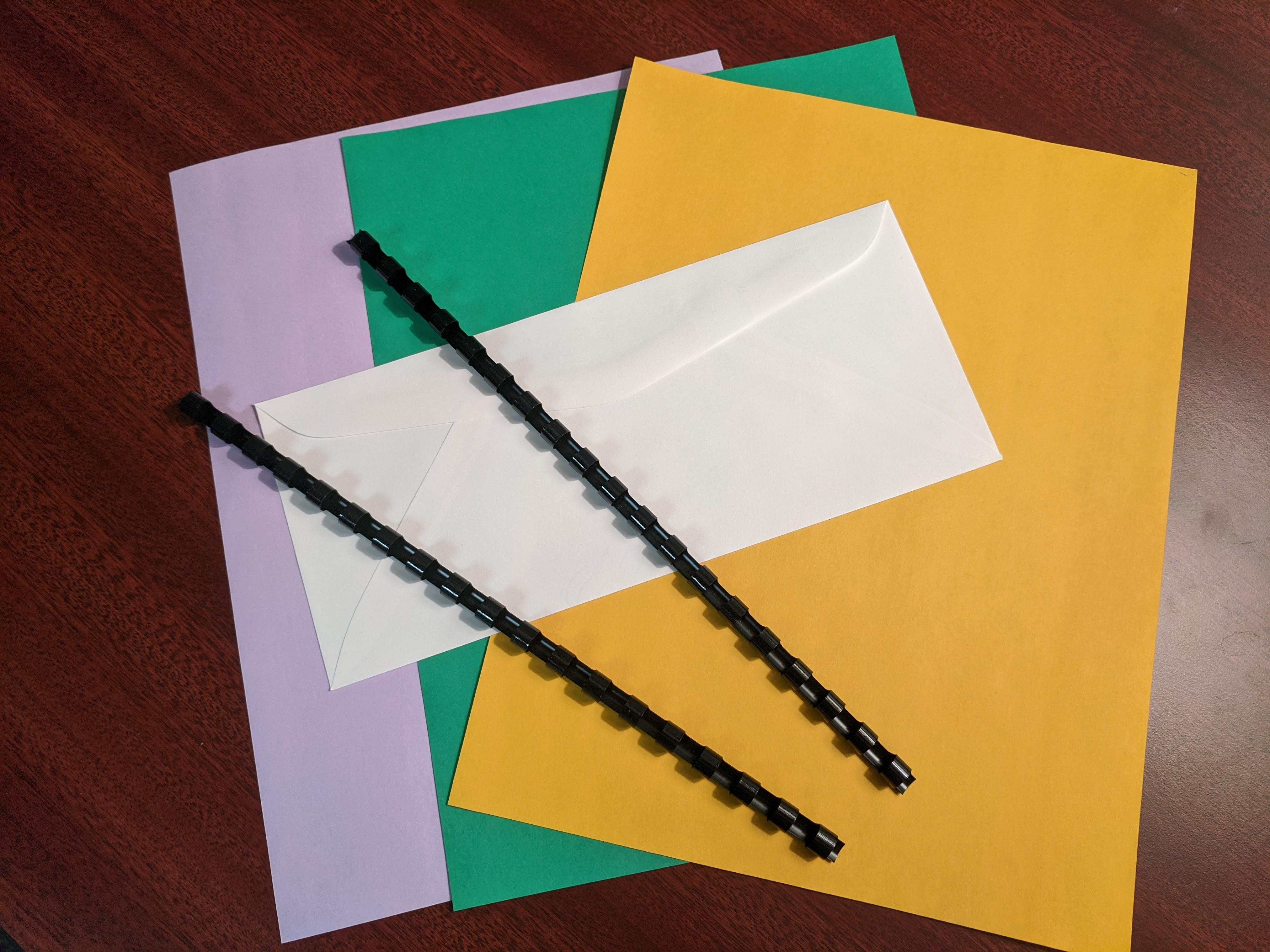 Sheets of colored paper, a blank envelope, and plastic combs used for binding pages