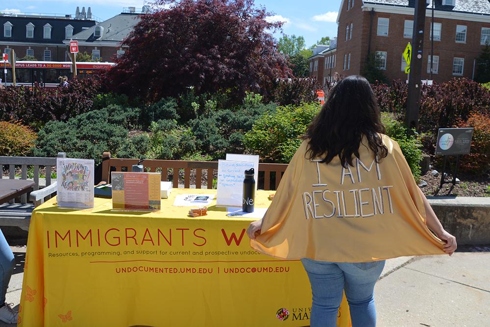 Student tabling outside Stamp Student Union wearing a cape that says resilient