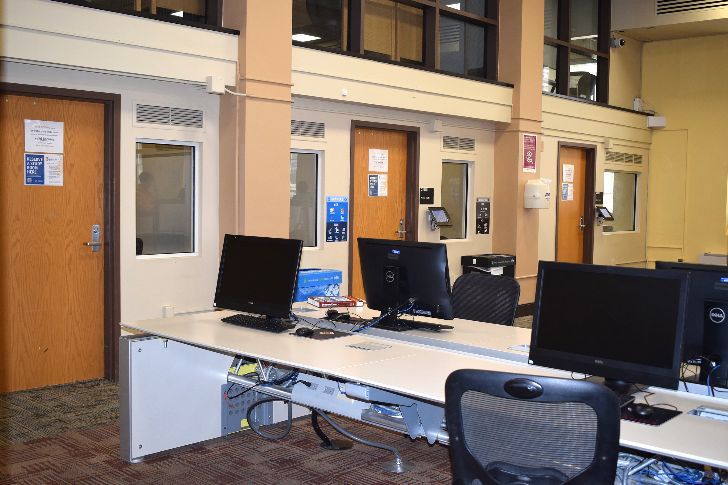 Rows of computers on a long table in front of the closed doors of three separate group study rooms