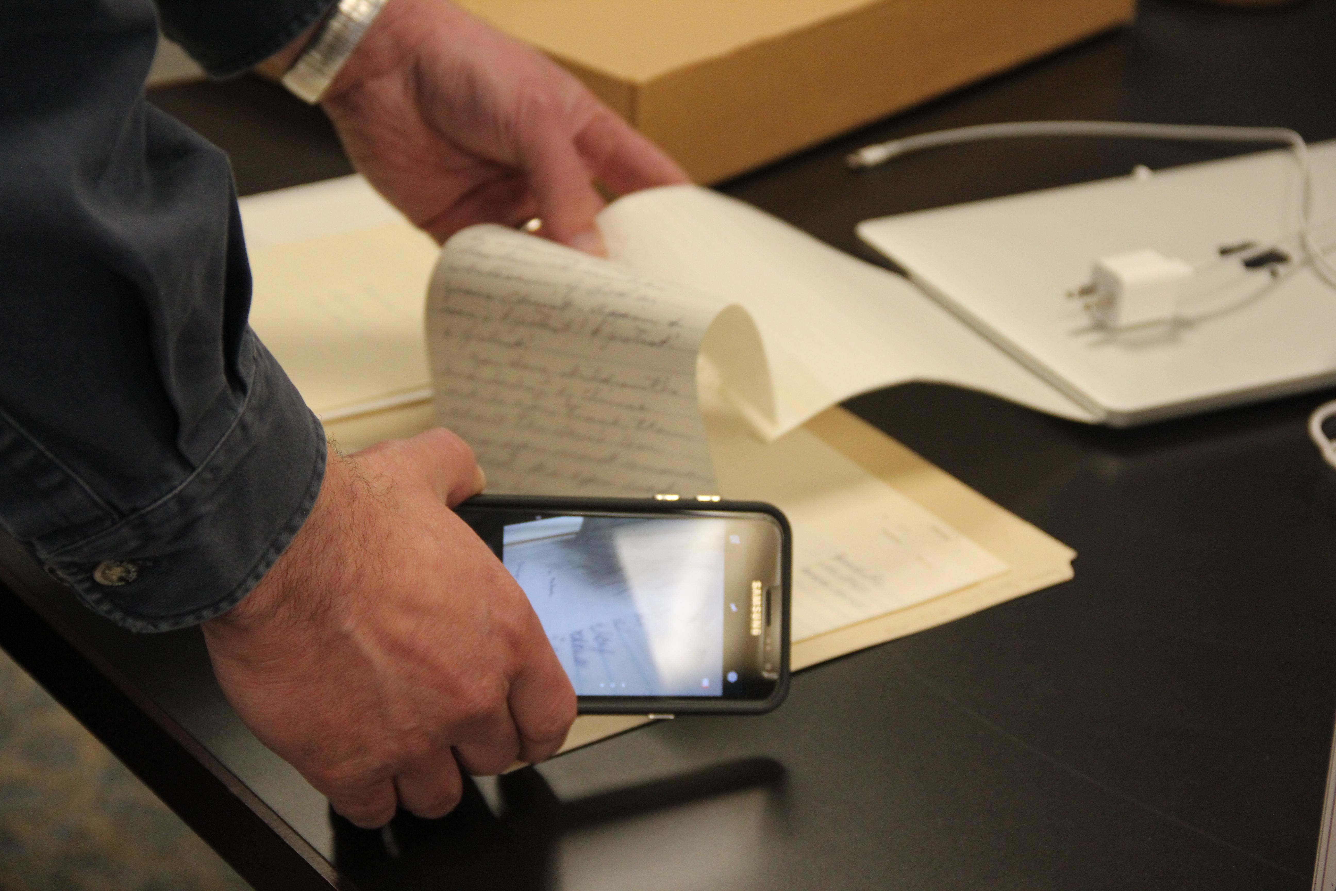 person holding cell phone with camera function open looking at documents