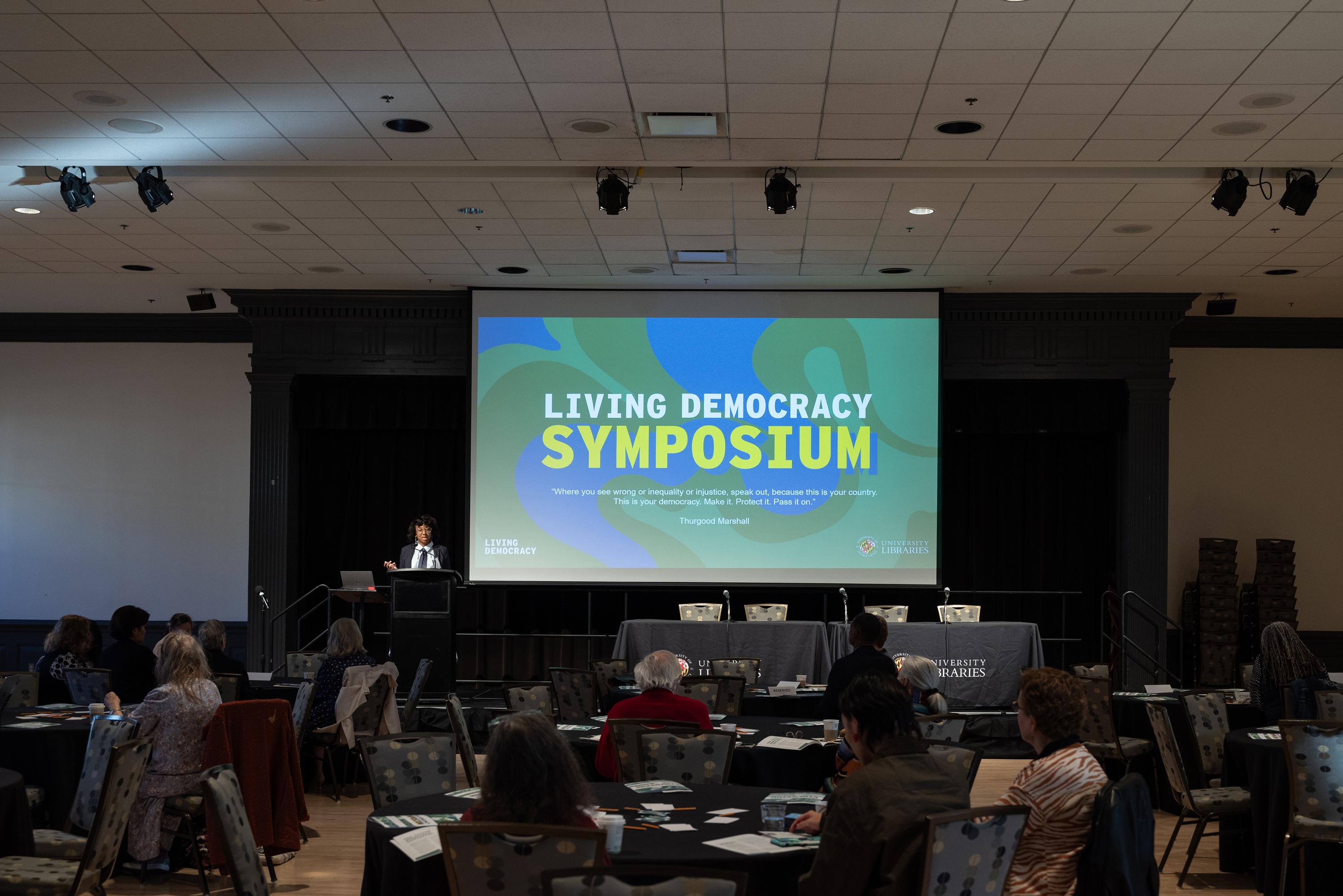 Wideshot from the back of the room of the crowd and stage at the Living Democracy Symposium.
