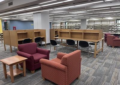 Carpeted open area with arm chairs, side tables and individual wooden desk stations and chairs. 