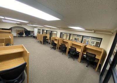 Carpeted room with individual wooden desk stations and chairs in rows.