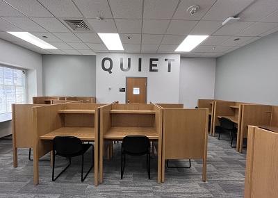 Carpeted room with individual wooden desk stations and chairs. 