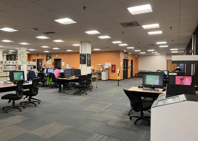 Open carpeted area with overhead scanners, computers and padded desk chairs with backs and wheels. 