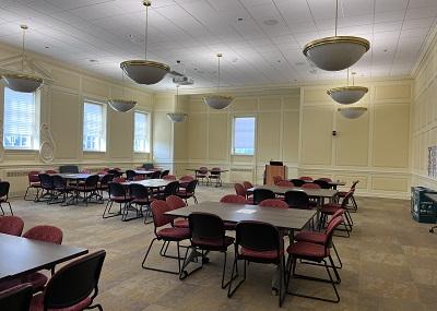 Carpeted windowed room, over head lit with wooden tables and padded chairs configured in small groups for a workshop